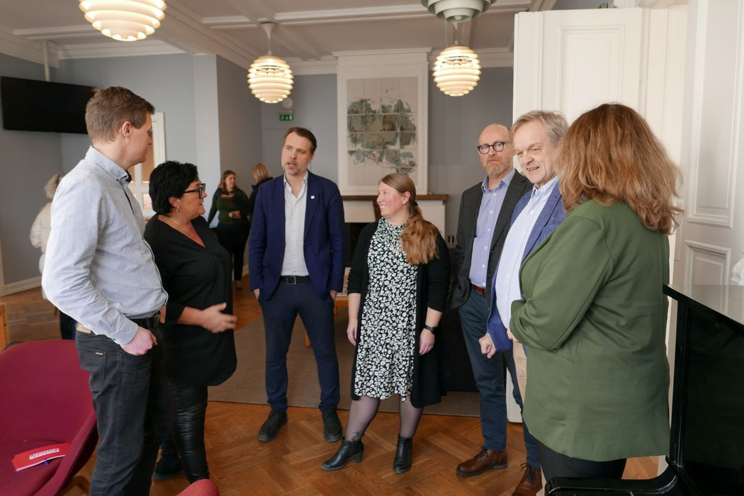 Gruppe på seks mennesker, tre kvinner og tre menn som står og snakker sammen.