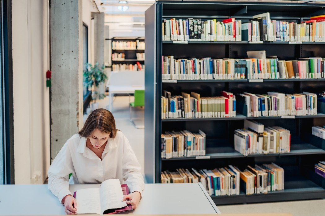 Kvinne som leser i bok på bibliotek