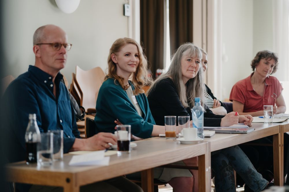 En mann og fire kvinner sitter ved et bord og noterer og følger med.