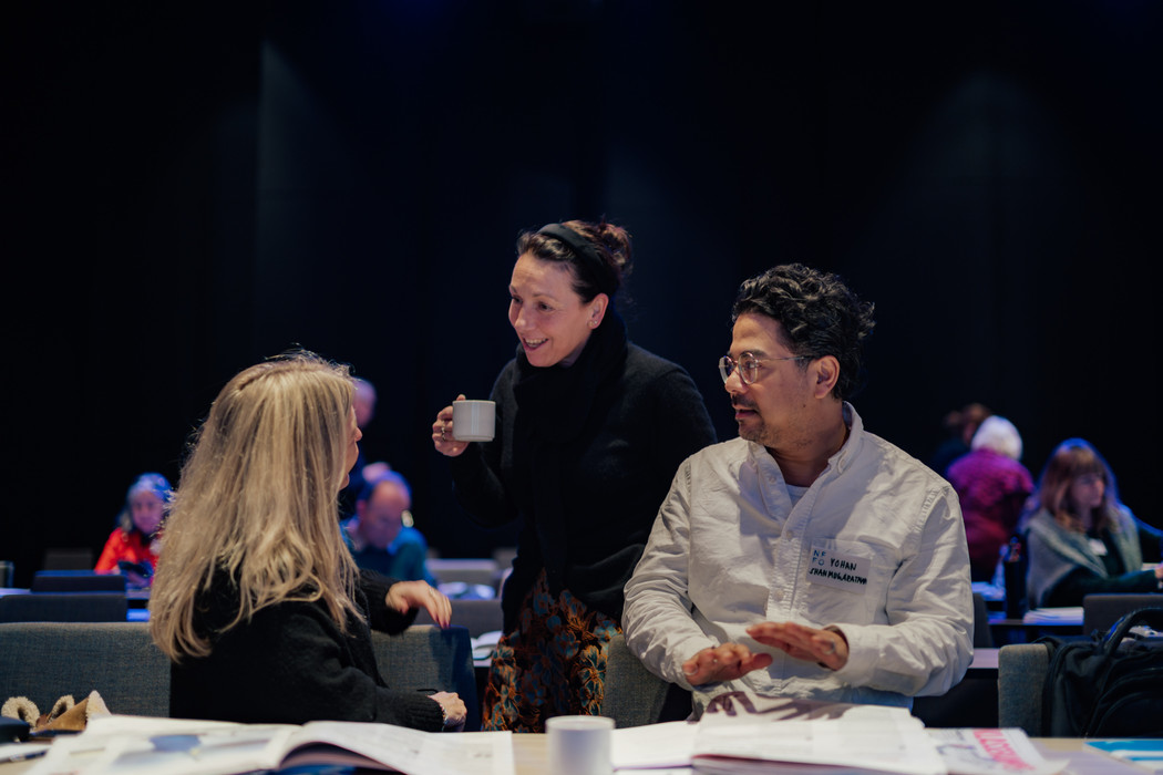 To kvinner og en mann som snakker sammen i en konferansesal.
