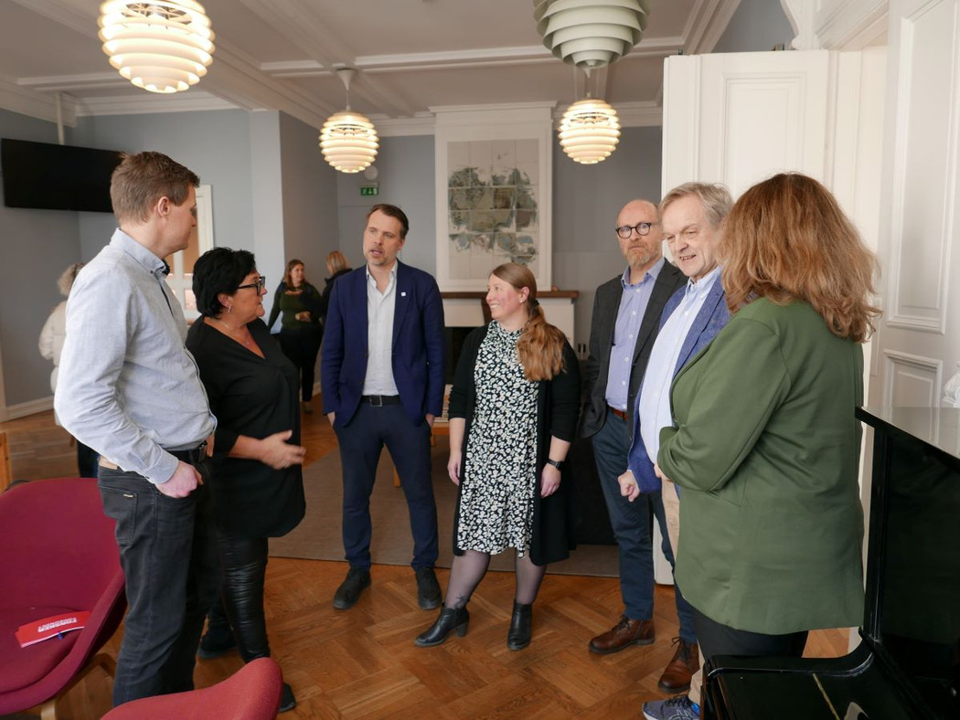 Gruppe på seks mennesker, tre kvinner og tre menn som står og snakker sammen.